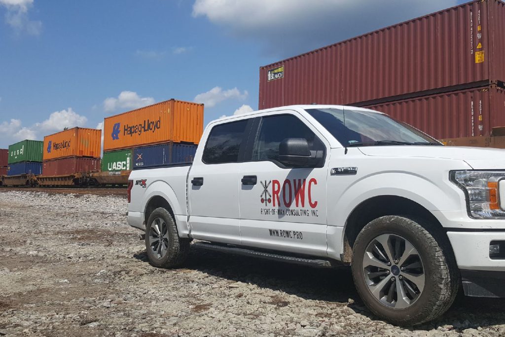 Right of Way Consulting truck at a rail yard with stacked shipping containers