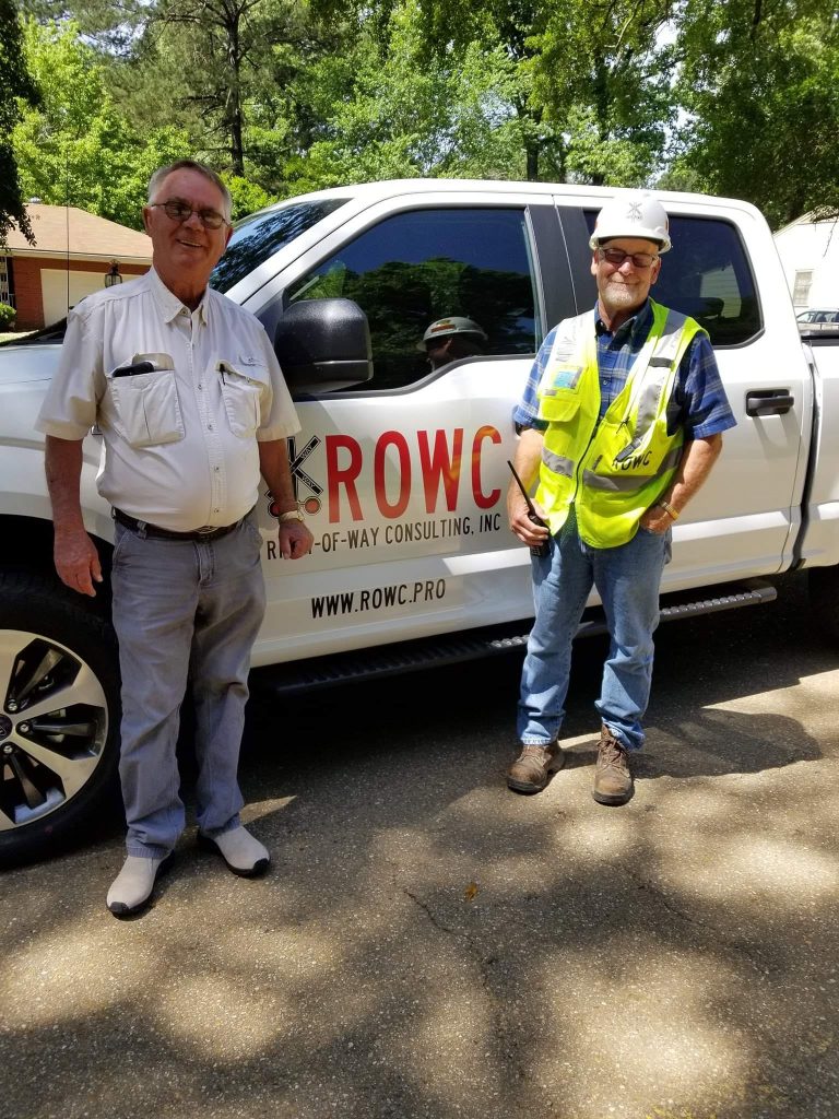 ROWC flagger and team member beside a Right of Way Consulting truck